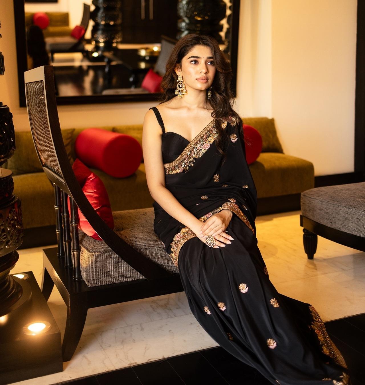 Krithi Shetty looks graceful in a beautiful black saree decorated with delicate golden embroidery. She pairs it with a simple black blouse, bold jhumkas, and a statement ring.